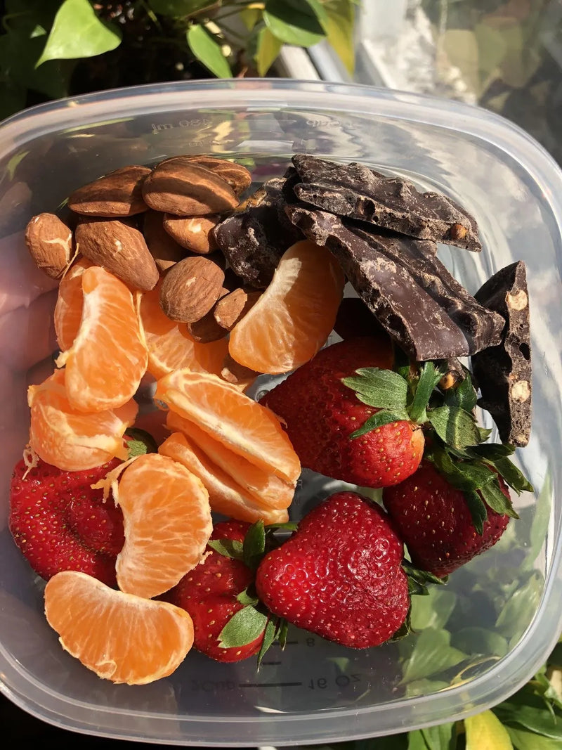 Tupper con fresas, naranja y chocolate como opciones para una alimentación saludable.